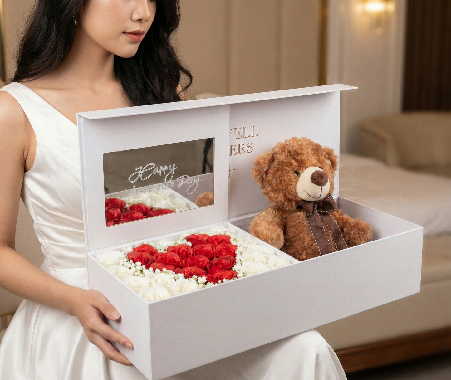 Woman holding a white gift box with a teddy bear and flower arrangement.