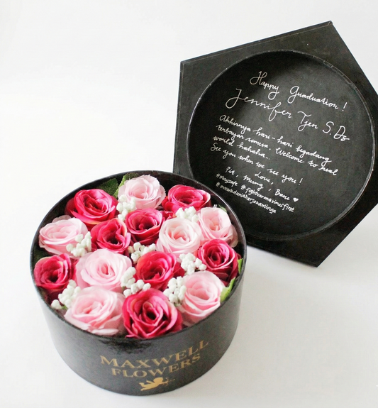 Round black box with pink and white flowers and a personalized message on a white background