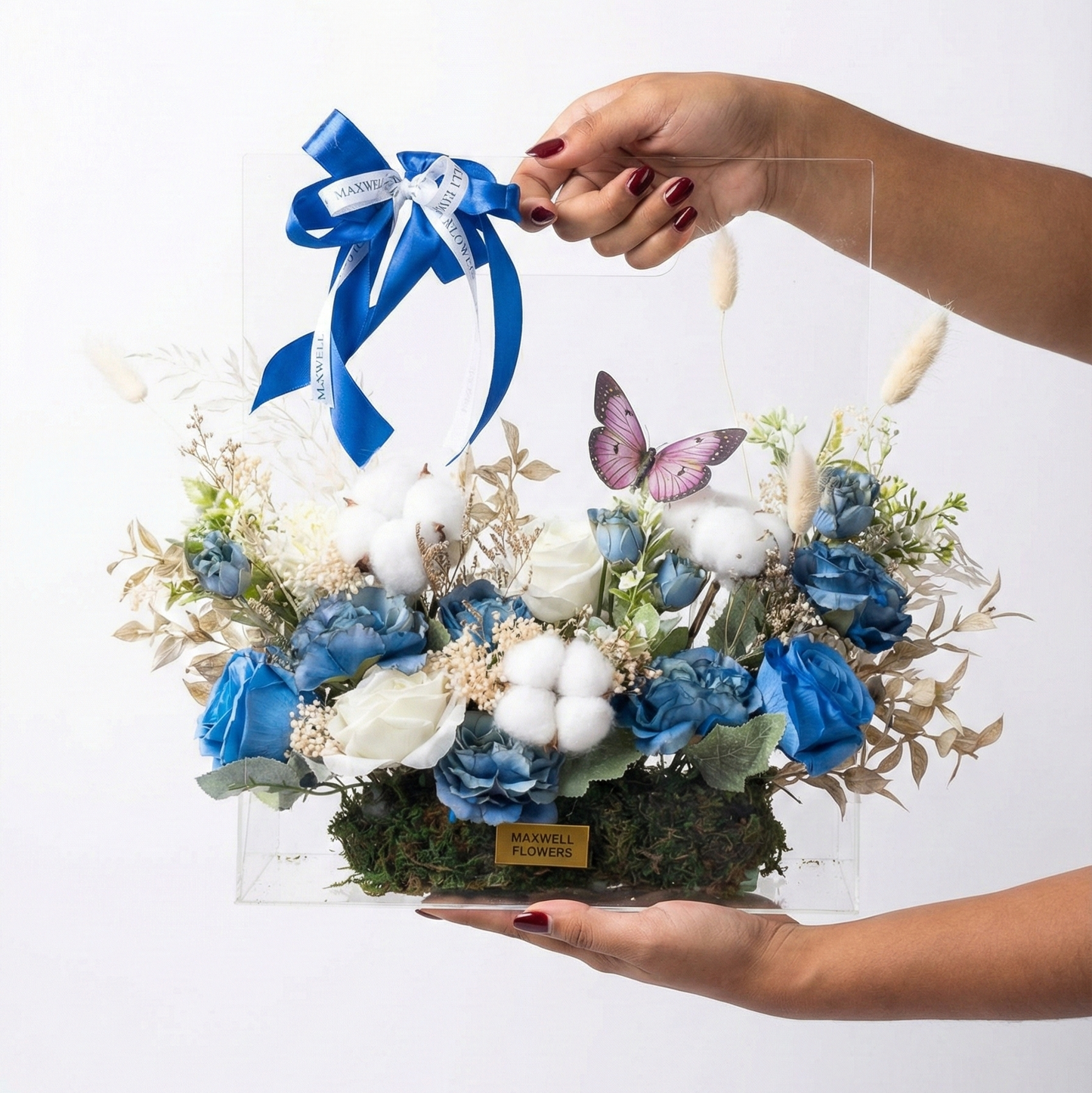 Floral arrangement with blue flowers and a blue ribbon held by hands on a white background