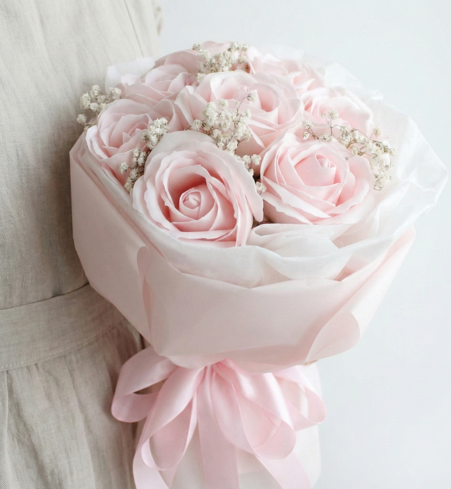 Bouquet of pink roses with a light pink ribbon held by a person wearing a beige dress.