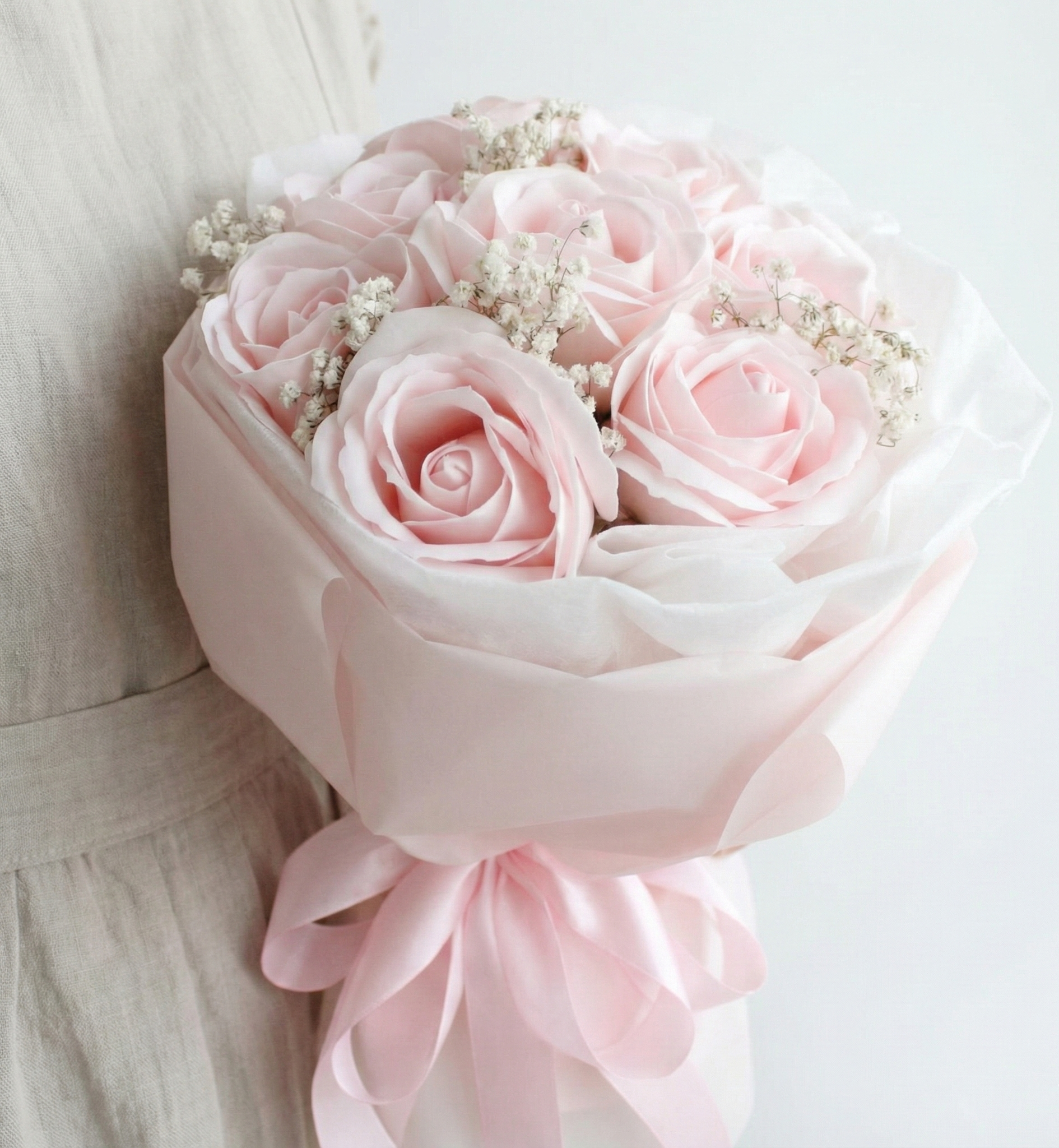 Bouquet of pink roses with a light pink ribbon held by a person wearing a beige dress.