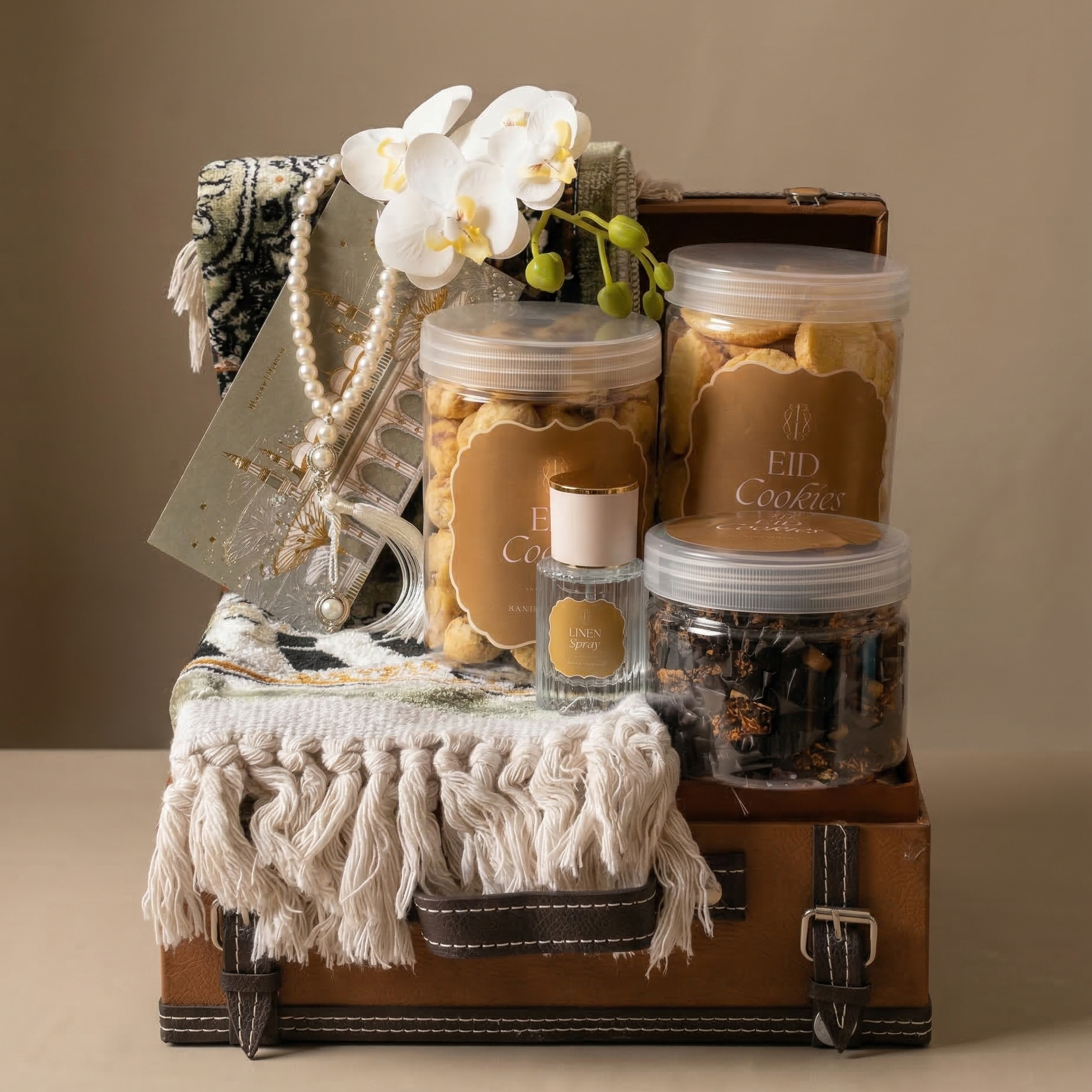 Gift set with cookies, flowers, and a bottle on a suitcase against a beige background