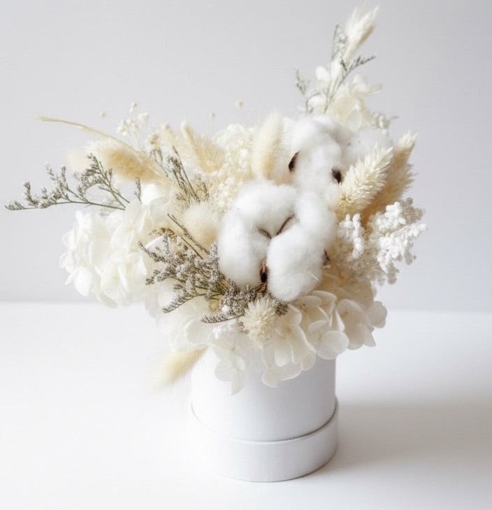 Bouquet of white flowers and cotton in a white vase on a light gray background