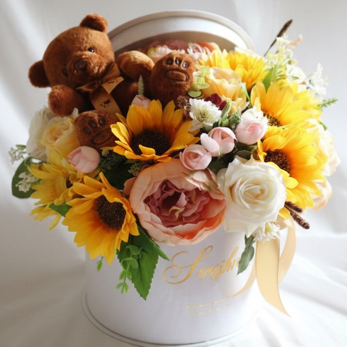 Floral arrangement with sunflowers, roses, and a teddy bear in a white container on a white background