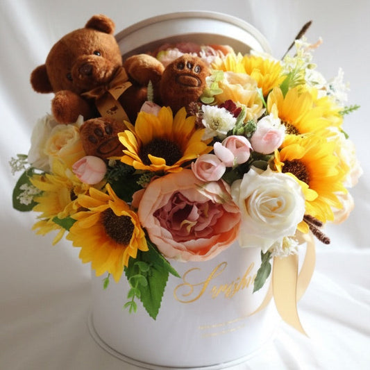Floral arrangement with sunflowers, roses, and a teddy bear in a white container on a white background