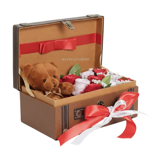 Brown suitcase with a teddy bear, flowers, and a red ribbon on a white background