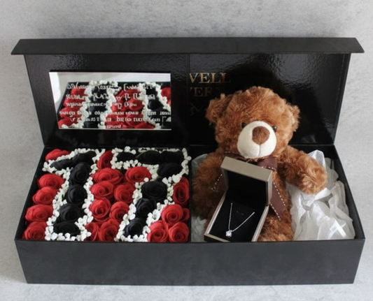 Gift set with teddy bear, chocolates, and flowers in a black box on a light gray background