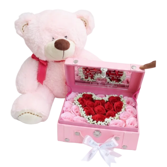 Pink teddy bear next to a pink jewelry box with heart-shaped rose arrangement on a white background
