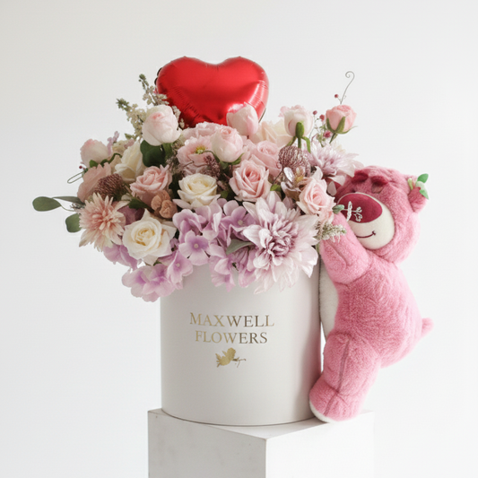Floral arrangement with a heart, teddy bear, and 'Maxwell Flowers' box on a white background